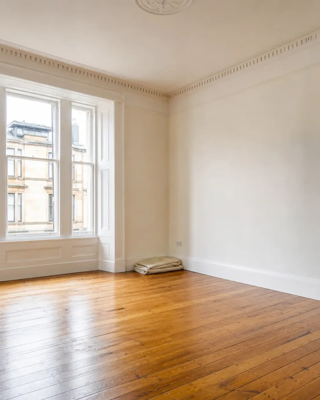 A stripped-back tenement room with a sash window, cornice ceiling and bare floorboards, cleared and ready for restoration work